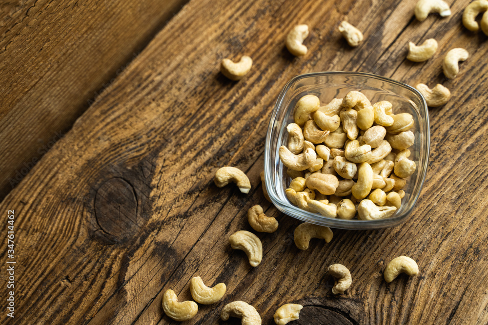 Cashew nuts in a small plate with scattered cashew around a plate on a vintage wooden table as a background. Cashew nut is a healthy vegetarian protein nutritious food. Cashew nuts in a small plate with scattered cashew around a plate on a vintage wooden table as a background. Cashew nut is a healthy vegetarian protein nutritious food.