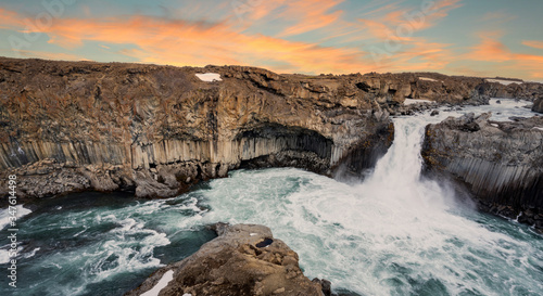Panorama of Aldeyjarfoss waterfall during sunset hours with pink streaky skies. Volcanic basalt textured rocky columns on the sides. Icelandic, travelling concept.