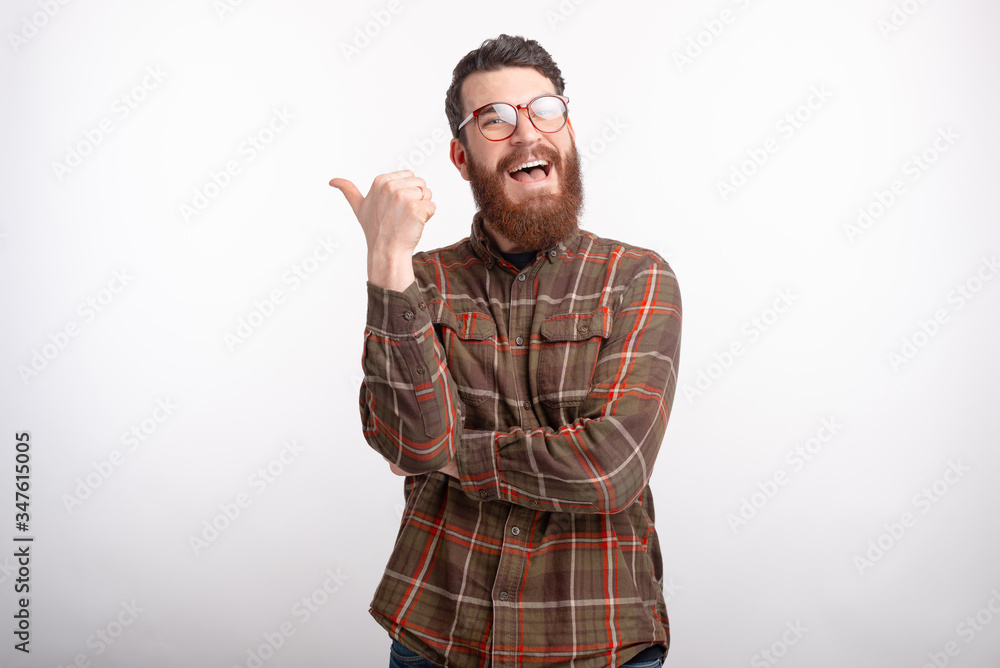 Cheerful bearded man is pointing with his thumb on the white background. Cheerful bearded man is pointing with his thumb on the white background.