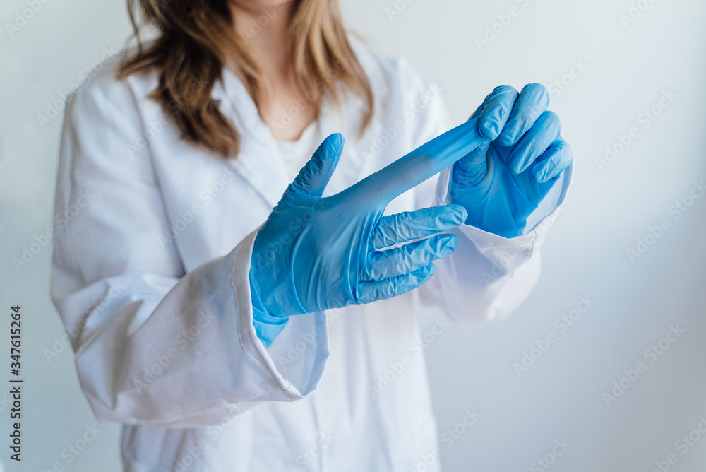 Young woman patient in a medical mask puts on protective surgical sterile gloves on her arm, isolated on gray background, protection against coronovirus Young woman patient in a medical mask puts on protective surgical sterile gloves on her arm, isolated on gray background, protection against coronovirus