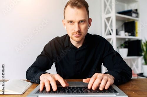 Webcam shot of young man in black casual shirt, he concentrated looks at the laptop screen, his hands on the keyboard. Freelancer, developer, writer at the work