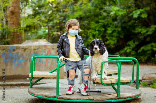 a little cool girl, walking a dog in the Playground, wearing a medical mask, during quarantine, because of the covid-19 pandemic