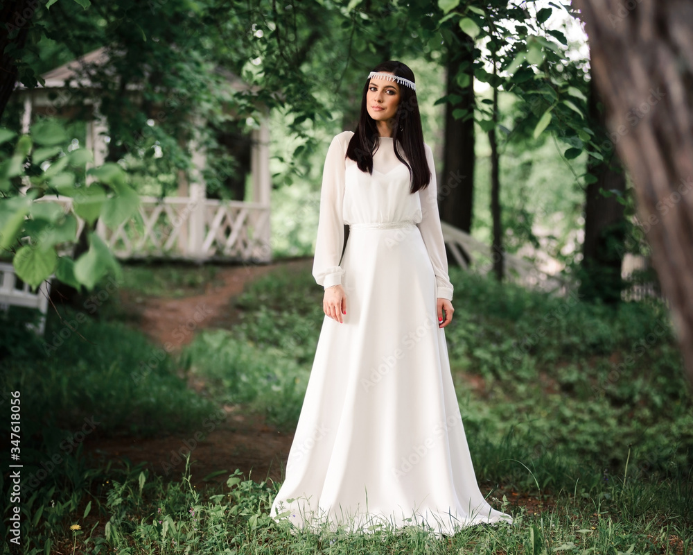 A summer wedding in the open air. The bride in an elegant wedding dress in a summer green garden against the background of a vintage white gazebo A summer wedding in the open air. The bride in an elegant wedding dress in a summer green garden against the background of a vintage white gazebo