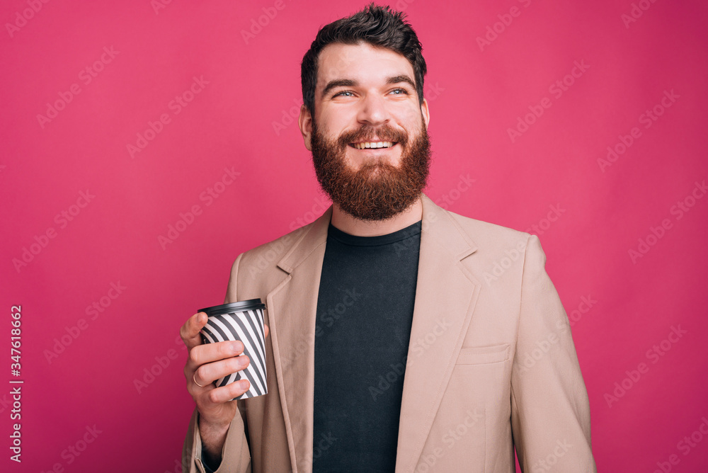 Dreaming bearded man is looking far while holding a paper cup over pink background. Dreaming bearded man is looking far while holding a paper cup over pink background.