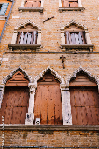 Windows of Venice are a building of several floors, made of red brick, three windows with brown shutters at bottom, two windows with wooden shutters-screen, stone columns and a sharp top by window