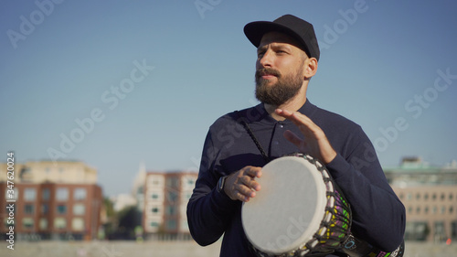 A street musician plays tom-tom on a drum. A musician stands on the street and holds a drum tomtom in his hands. photo