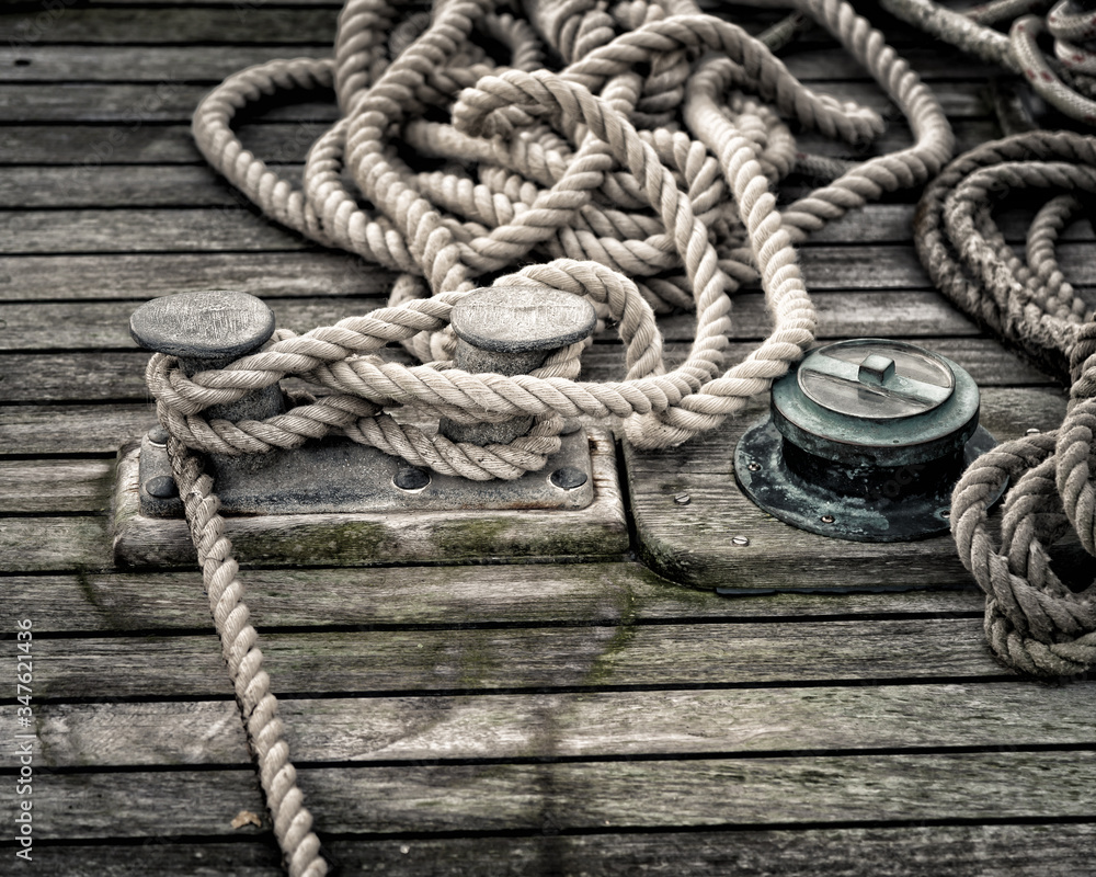 Obraz premium Three bollards on a wood deck with mooring lines rolled up around it