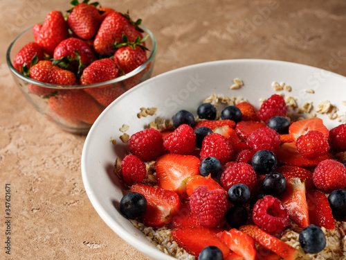 Oatmeal flakes breakfast with fresh berries - strawberry and blueberry  on homemade background and natural morning light.