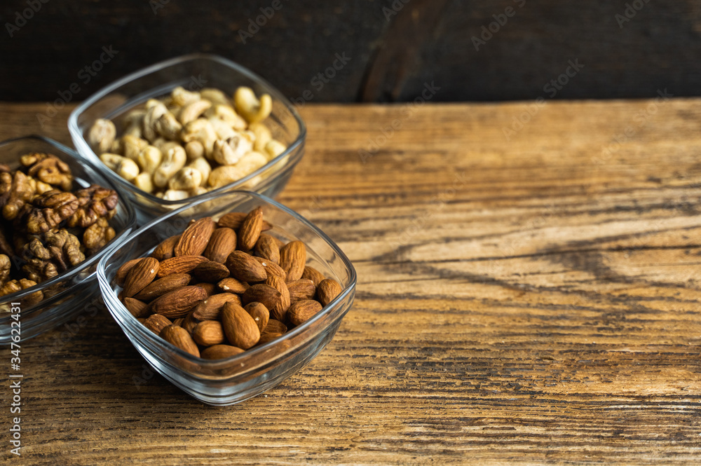 Almond, walnut and cashew in a small plates which standing on a wooden vintage table. Nuts is a healthy vegetarian protein and nutritious food. Nuts on rustic old wood. Almond, walnut and cashew in a small plates which standing on a wooden vintage table. Nuts is a healthy vegetarian protein and nutritious food. Nuts on rustic old wood.