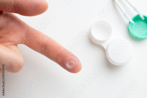 The man on the background of the containers for storing contact lenses and tweezers holding contact lens on finger