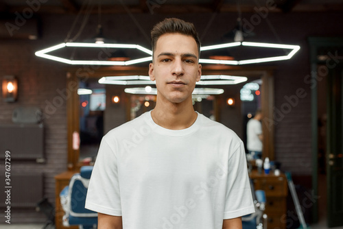I love my haircut. Portrait of a young handsome guy in white T-shirt with stylish haircut looking at camera while standing in barbershop