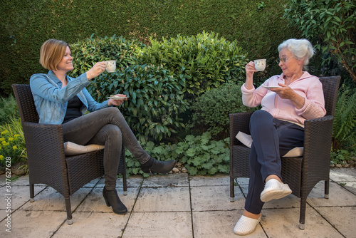 Senior woman and daughter having coffee at safety distance in the garden, 