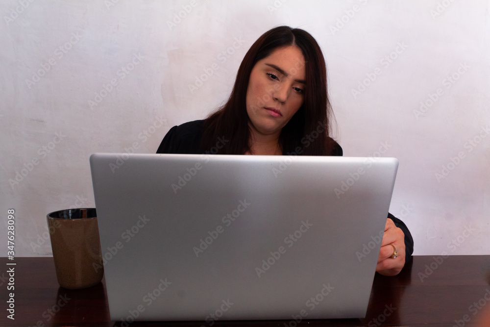Young Hispanic woman in black clothes doing home office with a white laptop in her dining room, typing and looking at her laptop Young Hispanic woman in black clothes doing home office with a white laptop in her dining room, typing and looking at her laptop