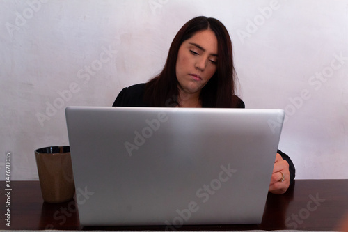 Young Hispanic woman in black clothes doing home office with a white laptop in her dining room, typing and looking at her laptop © Antonio Tanaka