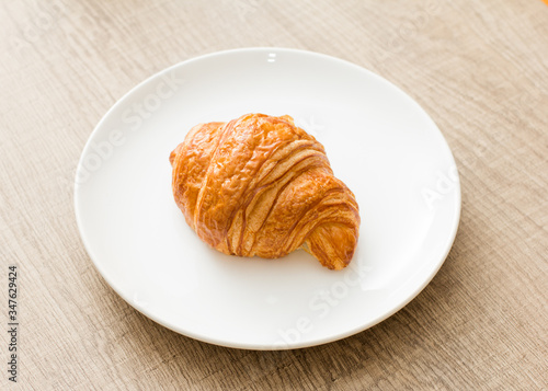 Food plate with croissant Dish showing bun of pastry. On rustic wooden table.