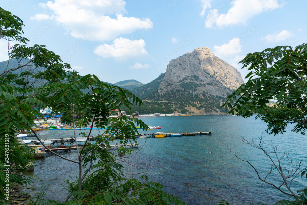 Sudak, New World, Russia - July 29, 2016: Panoramic view of the Black Sea coast. A pier with boats in the bay, view of Mount Sokol.