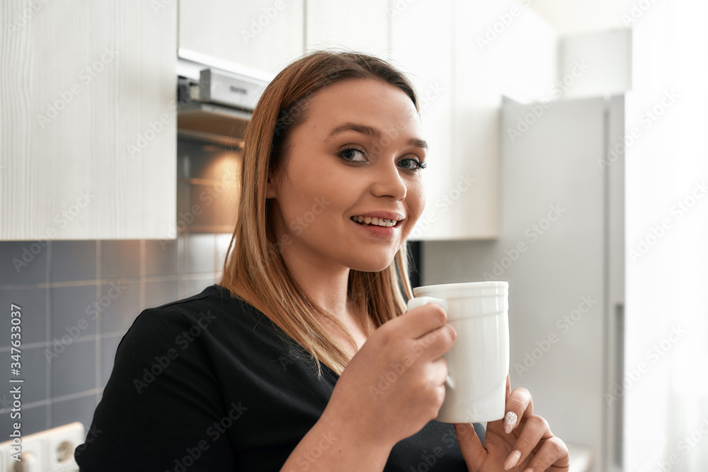 Coffee makes everything possible. Close up of young curvy woman looking at camera while drinking tea or coffee in the kitchen Coffee makes everything possible. Close up of young curvy woman looking at camera while drinking tea or coffee in the kitchen