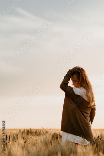 Young beautiful pregnant woman in white dress and jacket walking in the wheat orange field on a sunny summer day. Nature in the country. Miracle expectation. Sunset on isolation