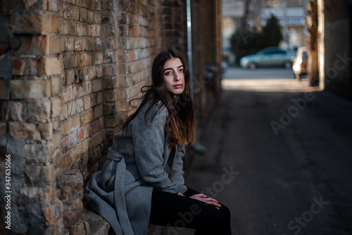 Girl in a red blouse and a gray cardigan on the background of the old brick wall © prokop.photo