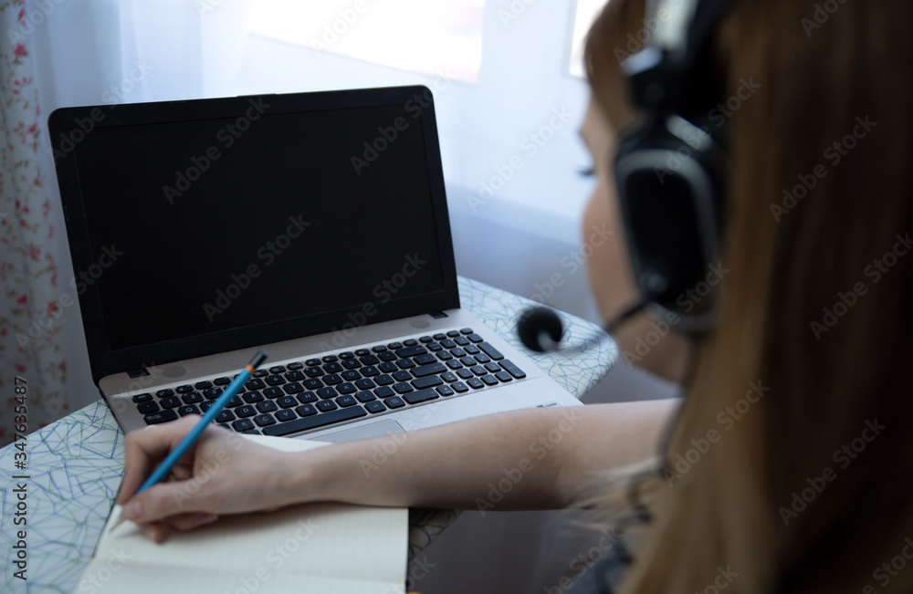 young american teen girl wear headphones video calling on laptop. pretty woman student looking at computer screen watching webinar or doing video chat by webcam young american teen girl wear headphones video calling on laptop. pretty woman student looking at computer screen watching webinar or doing video chat by webcam