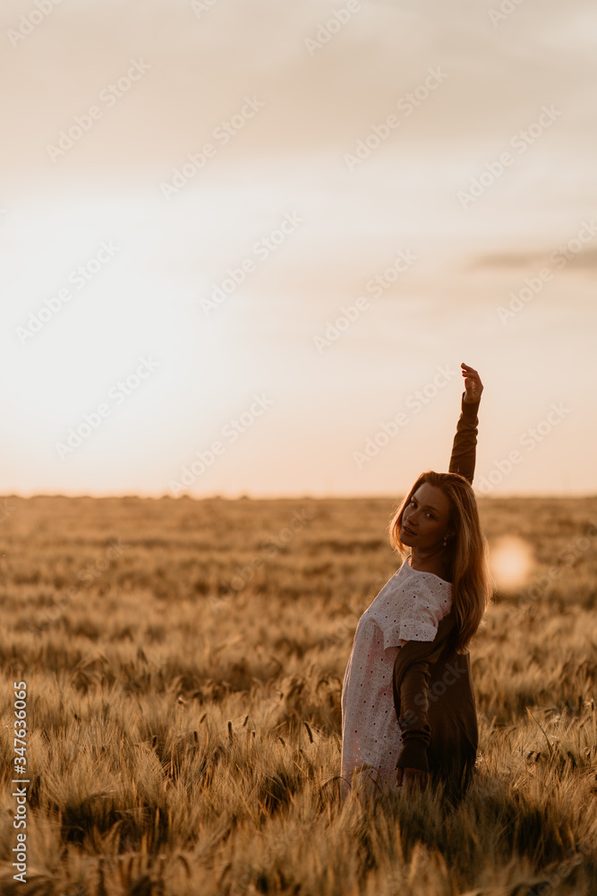 Young beautiful pregnant woman in white dress walking in the wheat orange field on a sunny summer day. Feel freedom with arm stretched to the sky. Miracle expectation. Sunset on isolation. Sun glare