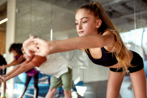 Make yourself fit. Portrait of a girl warming up, exercising together with other kids in gym. Sport, healthy lifestyle, active childhood concept