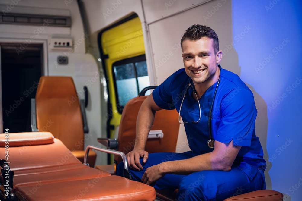 A portrait of a smiling man in a blue medical uniform sitting in the ambulance A portrait of a smiling man in a blue medical uniform sitting in the ambulance