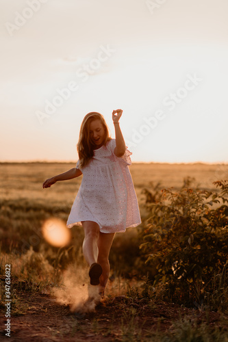Young beautiful woman making dust with her foot and screaming in the wheat orange field on a sunny summer day. Going crazy. Feeling free and happy. Miracle expectation. Sunset on isolation. Sun glare