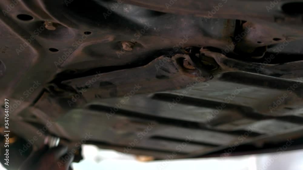 An auto mechanic screws crankcase protection with a pneumatic wrench in the service station. Close-up bottom of lifted car. Dirty hands of mechanic. An auto mechanic screws crankcase protection with a pneumatic wrench in the service station. Close-up bottom of lifted car. Dirty hands of mechanic.
