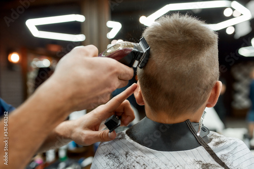 Haircuts for Kids. Barber making haircut with electric hair clipper for little boy at barber shop. Using a trimmer. Shaving a hair from the back of the head