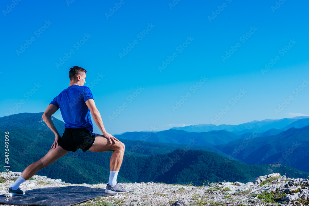 Blonde athlete wearing blue dry-fit shirt stretching and preparing for a workout while standing on top of a cliff which has an amazing view. Blonde athlete wearing blue dry-fit shirt stretching and preparing for a workout while standing on top of a cliff which has an amazing view.