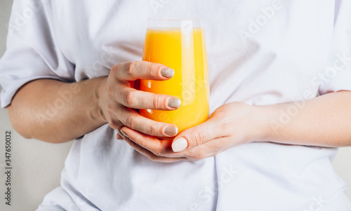 Female hands with glass of orange juice. Woman in white t-shirt. Healthy breakfast and stay at home concept.