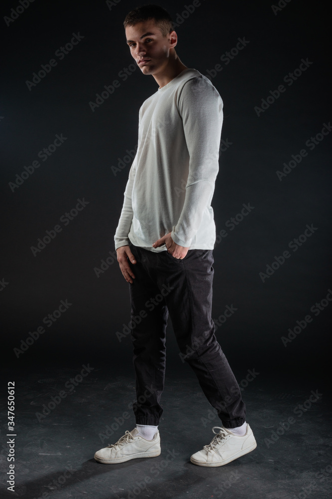 Fashion portrait on a black background of a handsome male model in white blouse and black pants Fashion portrait on a black background of a handsome male model in white blouse and black pants