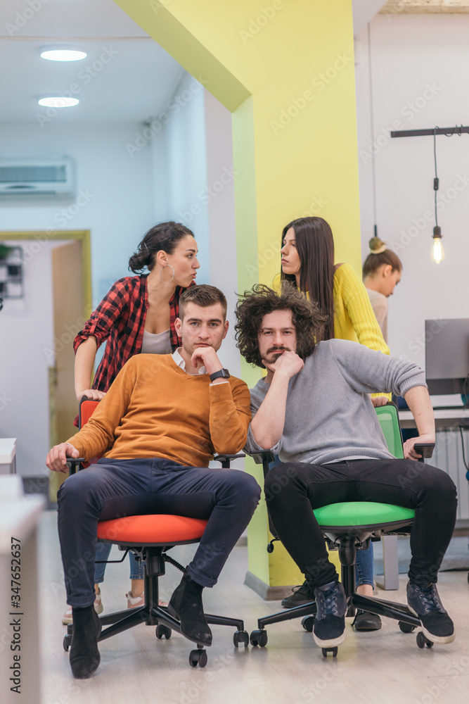 Team building and office fun.Four young cheerful businesspeople in smart casual wear having fun while racing on office chairs and smiling.. Team building and office fun.Four young cheerful businesspeople in smart casual wear having fun while racing on office chairs and smiling..