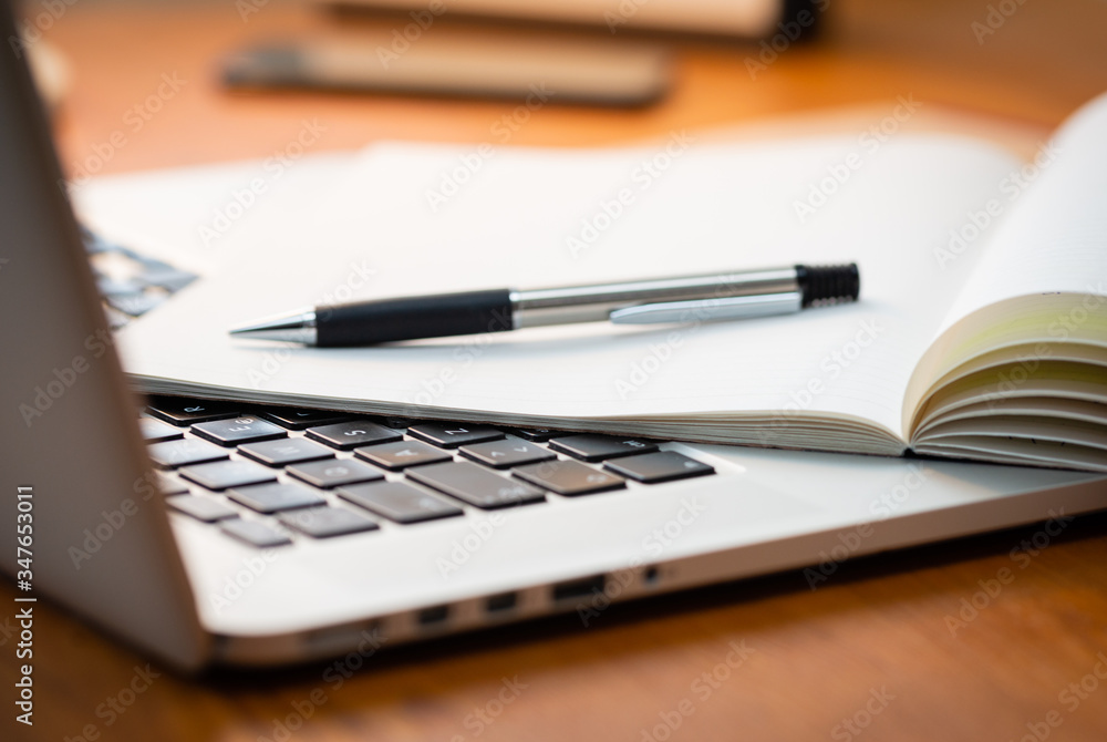 Laptop Computer on a Modern Wooden Business Desk with a Notepad and Pen in Unfocused Background. Laptop Computer on a Modern Wooden Business Desk with a Notepad and Pen in Unfocused Background.