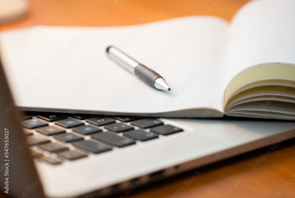 Laptop Computer on a Modern Wooden Business Desk with a Notepad and Pen in Unfocused Background. Laptop Computer on a Modern Wooden Business Desk with a Notepad and Pen in Unfocused Background.
