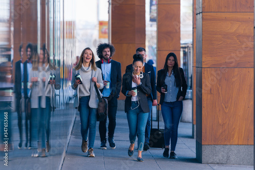 Full length of a group of colleagues in casual businesswear discussing business while walking at office hall. © qunica.com