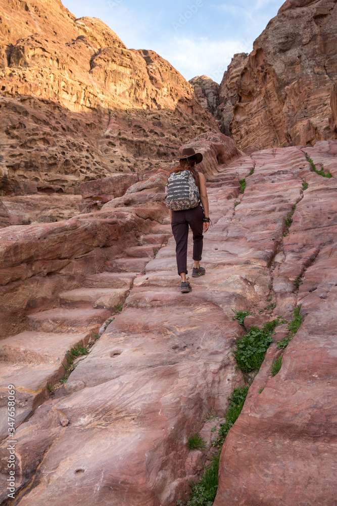 Girl tourist with a backpack and a cowboy hat climbs the ancient stairs carved into the mountains.