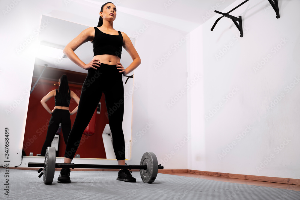 Confident fit young woman standing in gym and working out with weights 