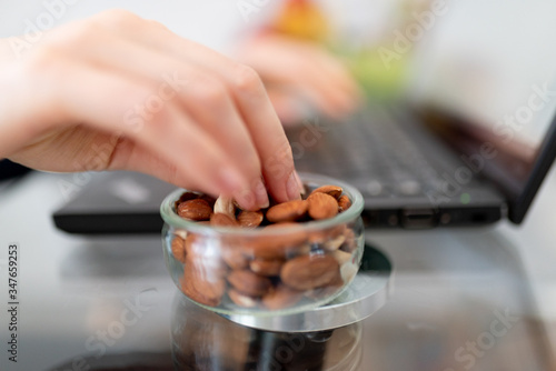 The woman works remotely, using a laptop, eating peanuts with her hands. Hands eating
