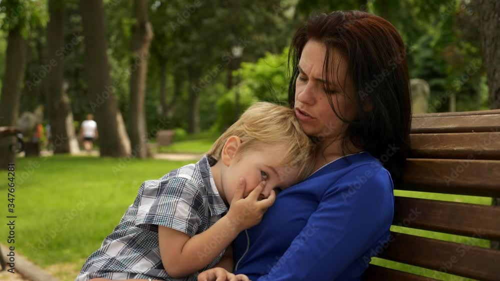 Mother Sits with Child on Bench in City Park. Urban Green Space. Bright Sunny Summer Day Mother Sits with Child on Bench in City Park. Urban Green Space. Bright Sunny Summer Day