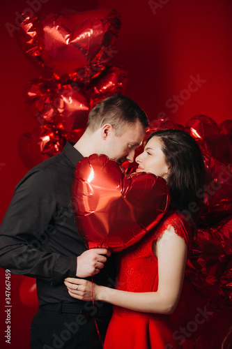 Loving couple with red balloons hearts. Man and woman celebrate valentine's day. Romantic date on a red background. Boyfriend and girl have fun on holiday.