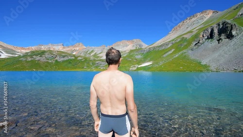 Back of fit man swimming standing in cold colorful water of Ice Lake on trail in Silverton, Colorado in San Juan Mountains in summer seamless loop photo