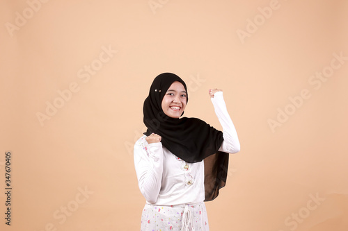 Portrait of happy young Muslim Asian Girl laughing hard with big open mouth, over orange background. Indonesian woman © Mohammad