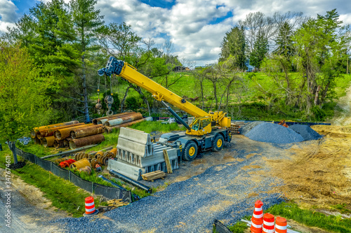 Aerial view of yellow heavy duty jib equipped  telescopic crane at a road widening construction site with boom nose surrounded by rusty steel pipes and concrete road blocks  photo