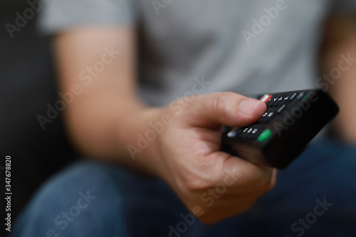 The hand is pressing the remote control to select the channel.Spend leisure time at home watching a movie.