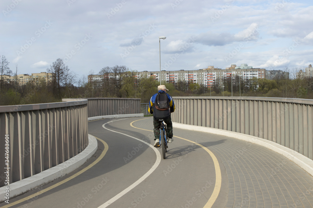 An elderly male cyclist dressed in beautiful modern sportswear rides a bicycle on a special bike path across the bridge in the city.