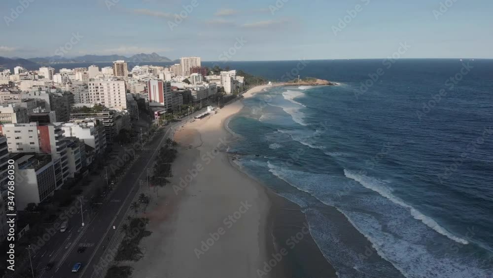 Long waves coming in on an almost empty Ipanema beach in shadow in late afternoon with the Arpoador rock in the background during the COVID-19 Corona virus outbreak after a tidal wave Long waves coming in on an almost empty Ipanema beach in shadow in late afternoon with the Arpoador rock in the background during the COVID-19 Corona virus outbreak after a tidal wave