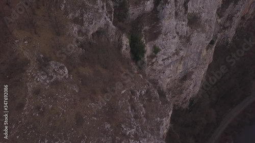 Bright red jacket of climber high on cliff face is barely visible against the steep rugged terrain. Aerial view of Casa Zmeului and people enjoying rock climbing in this protected park of Romania. photo