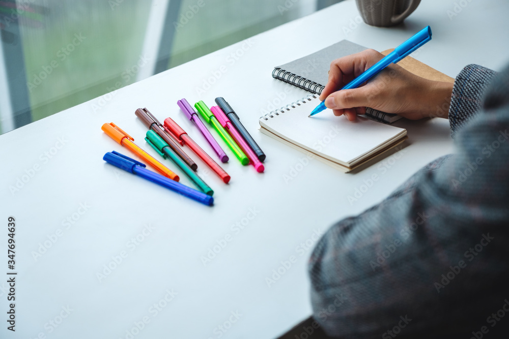 Closeup image of a woman writing on a blank notebook with colored pens on the table Closeup image of a woman writing on a blank notebook with colored pens on the table